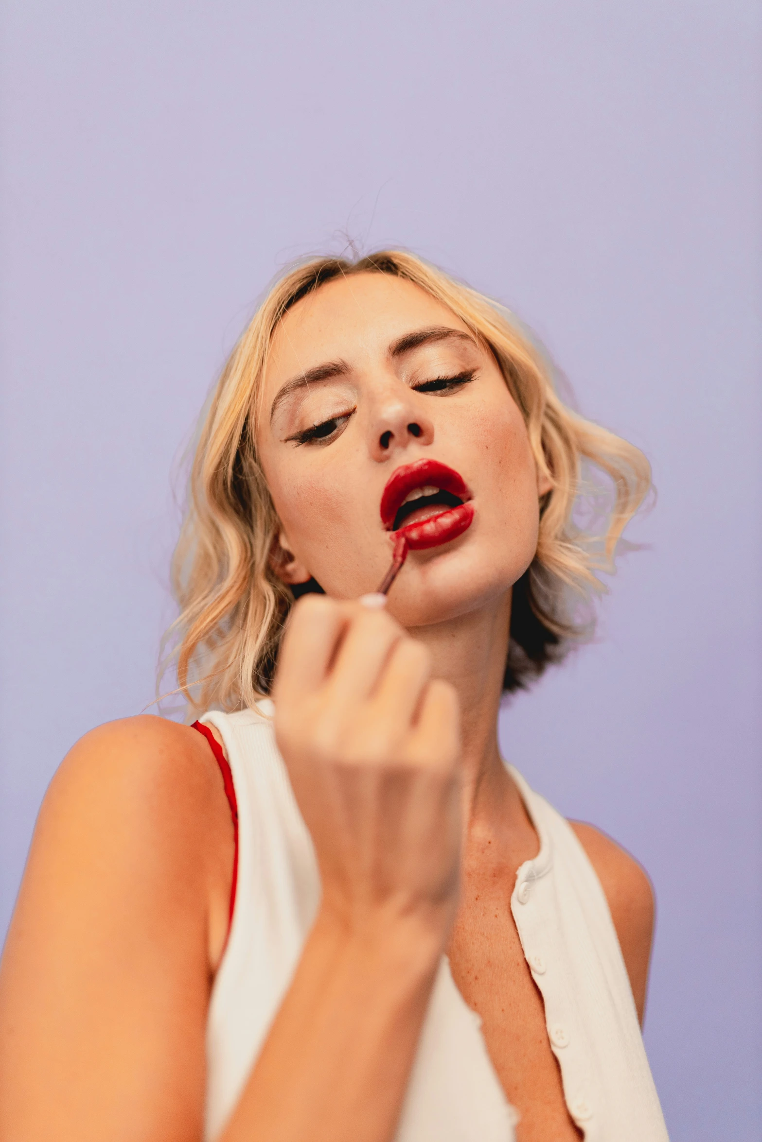 young woman putting lipstick on her cheek to show tongue