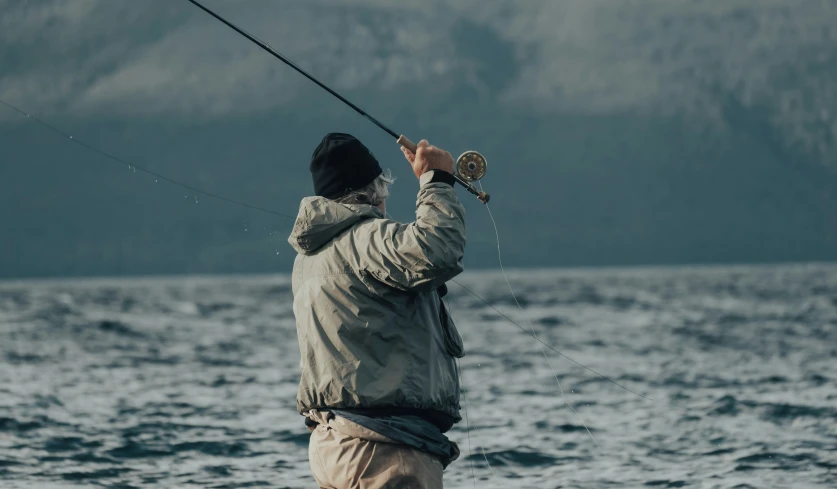 a man standing on the edge of a body of water fishing