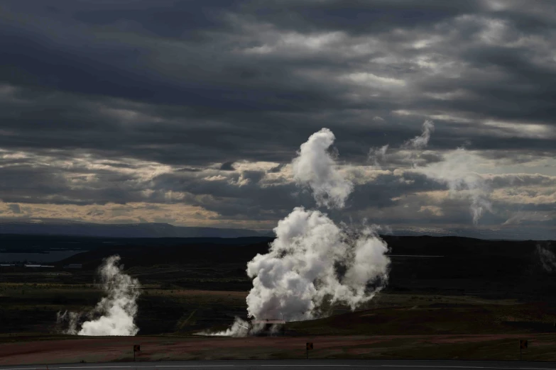 three white smokes rising from the ground with cloudy skies in the background