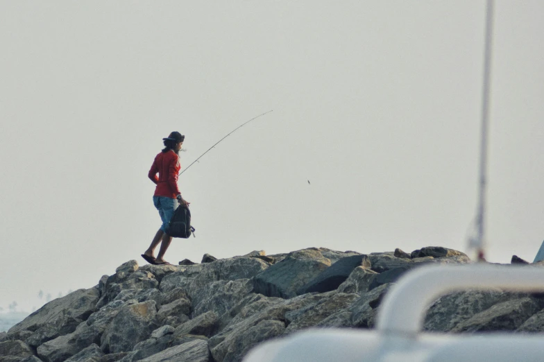 a person stands atop rocks fishing in the ocean