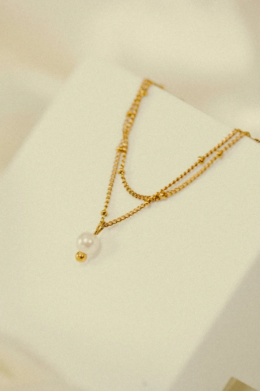 a yellow gold necklace hanging on top of a white box