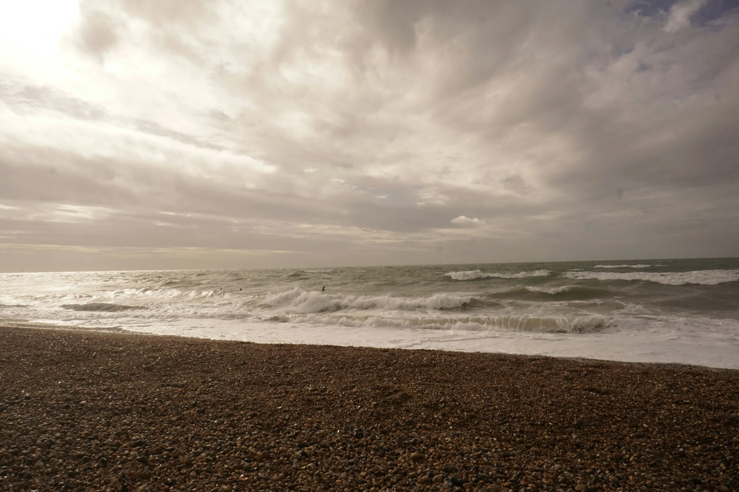 waves come in to the beach as a person walks on the sand