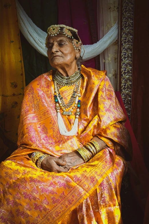 an old woman wearing bright orange is sitting on a chair