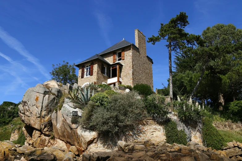 a house on a rocky hill that has trees on it