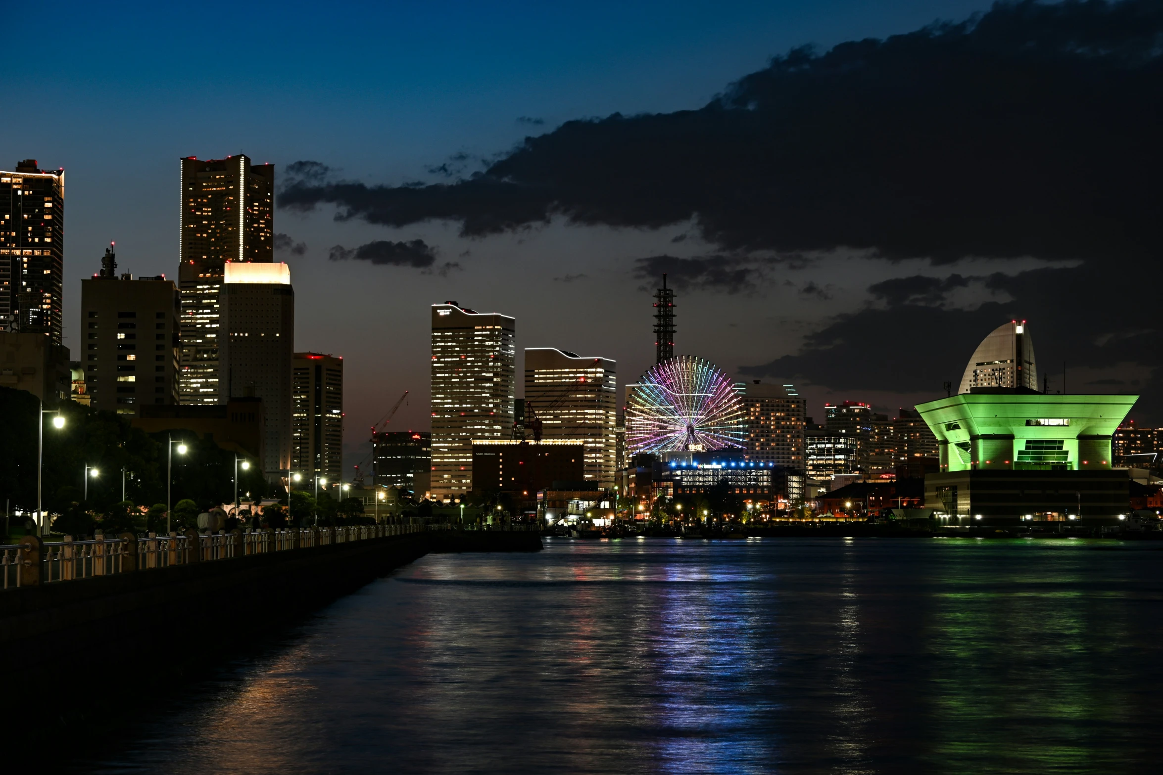 city skyline and ferris wheel reflected in water at night