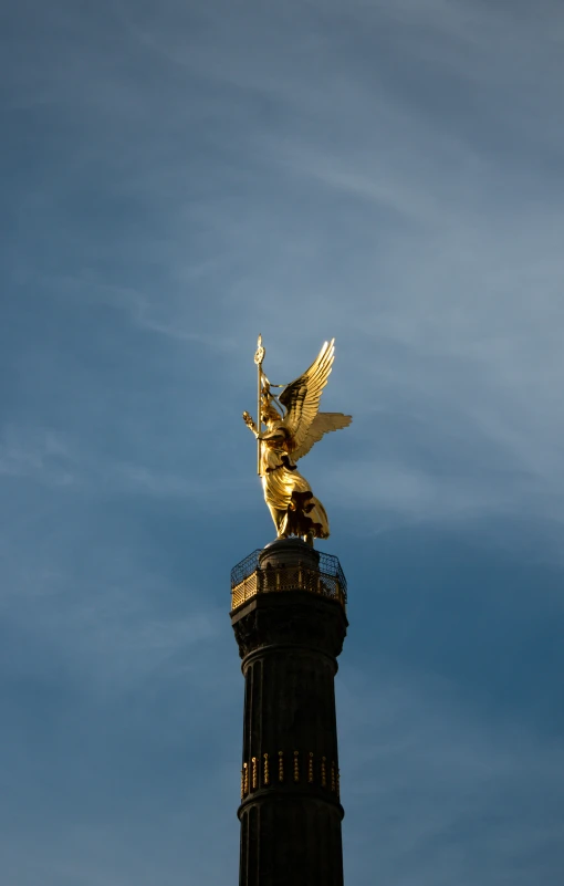 a golden statue atop a bronze tower with a light at the top