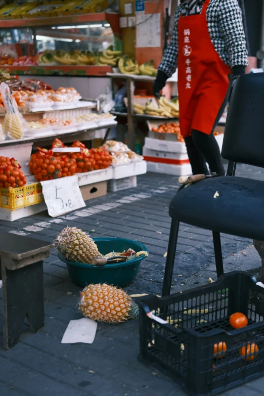 a large chair sits on the ground in front of an outdoor fruit stand