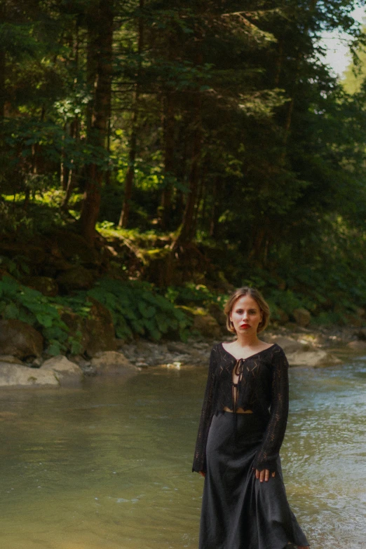 the woman in the long dress is standing near a stream