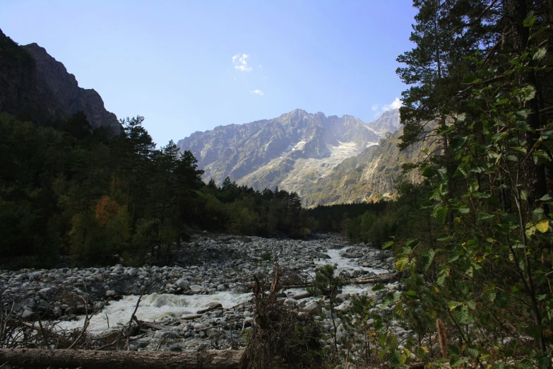 a river running through a forest under tall mountains