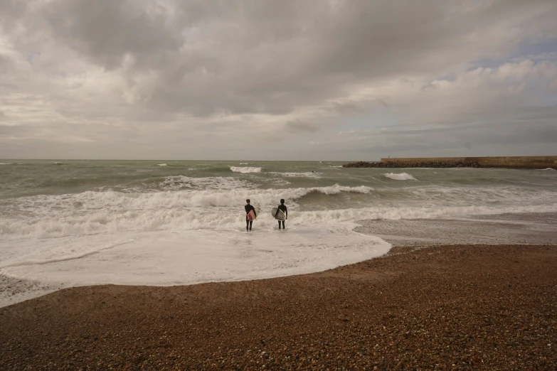 two people walk into the ocean as waves come in