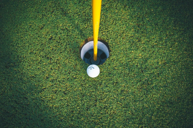 a white ball laying under a yellow pole in the grass