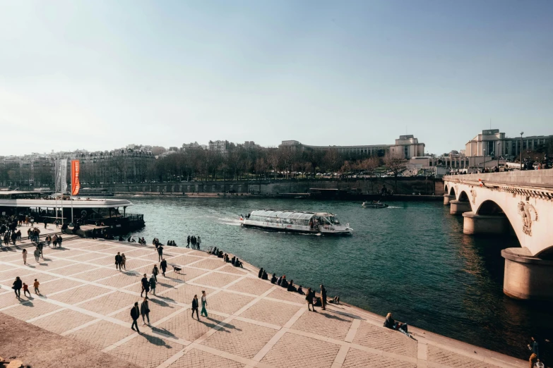 people walking and sitting along the waterfront of a river