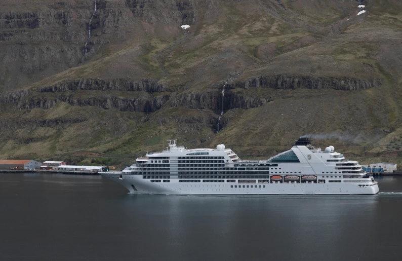 large cruise ship moored near a mountain and pier