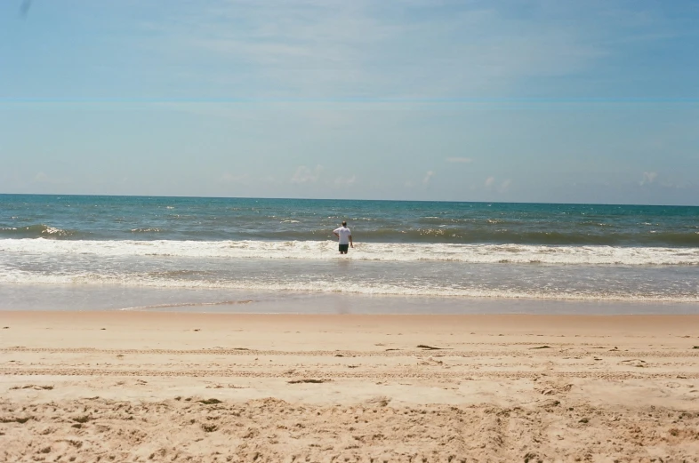 a man standing in the ocean on top of a sandy beach