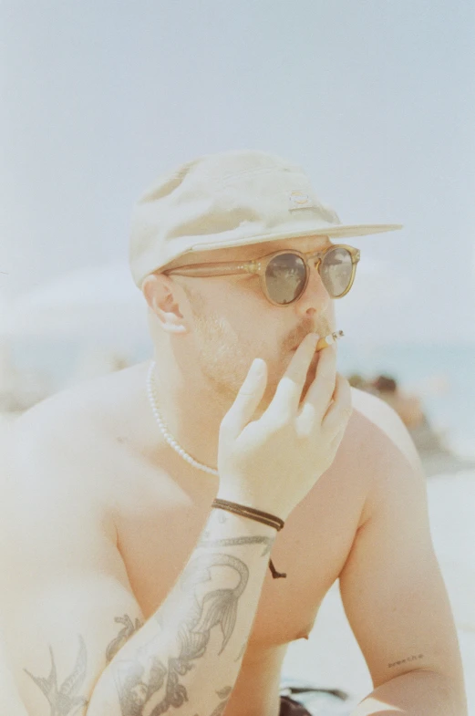 a man in a cap and sunglasses smoking cigarette on a beach