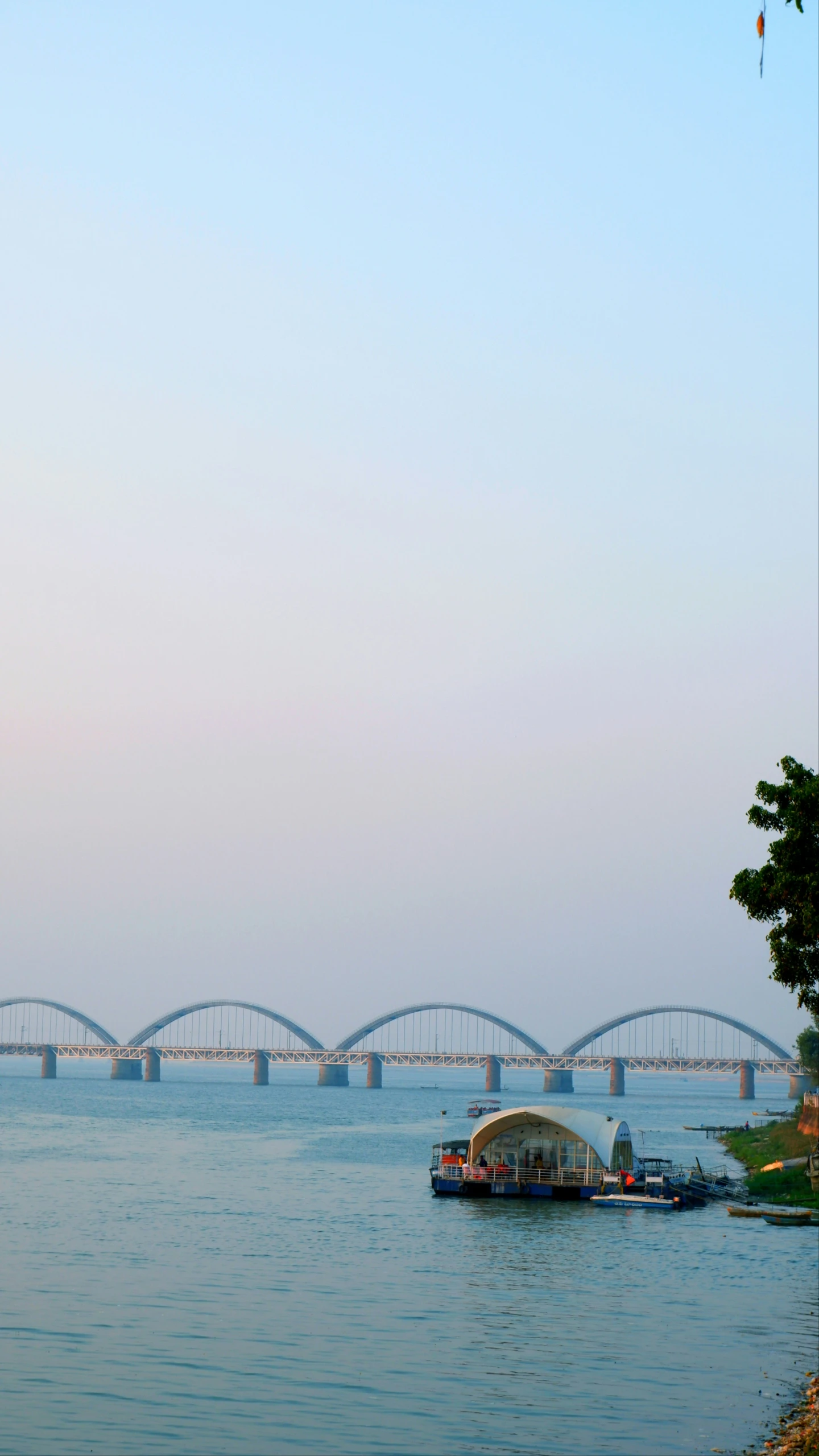 people fly kites on a sunny day next to a long bridge