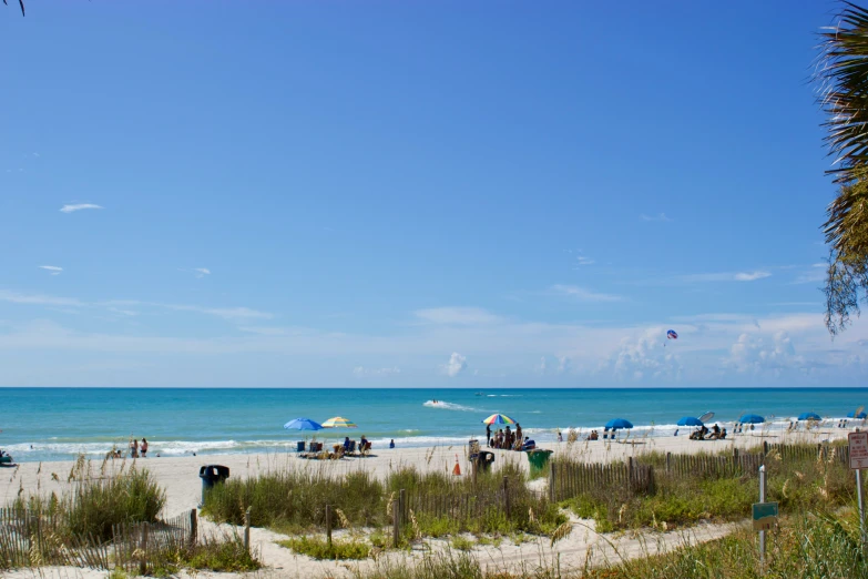 the beach has people on it and many have blue umbrellas