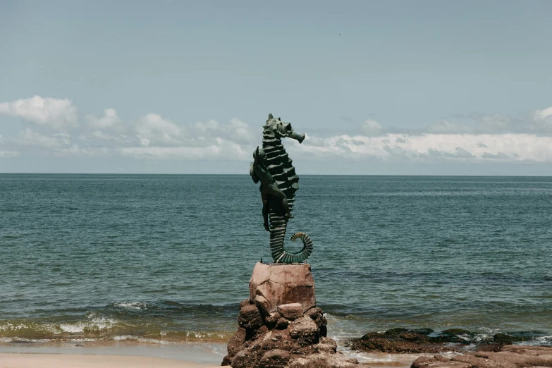 a bronze statue of a seahorse sitting on top of a rock near the ocean