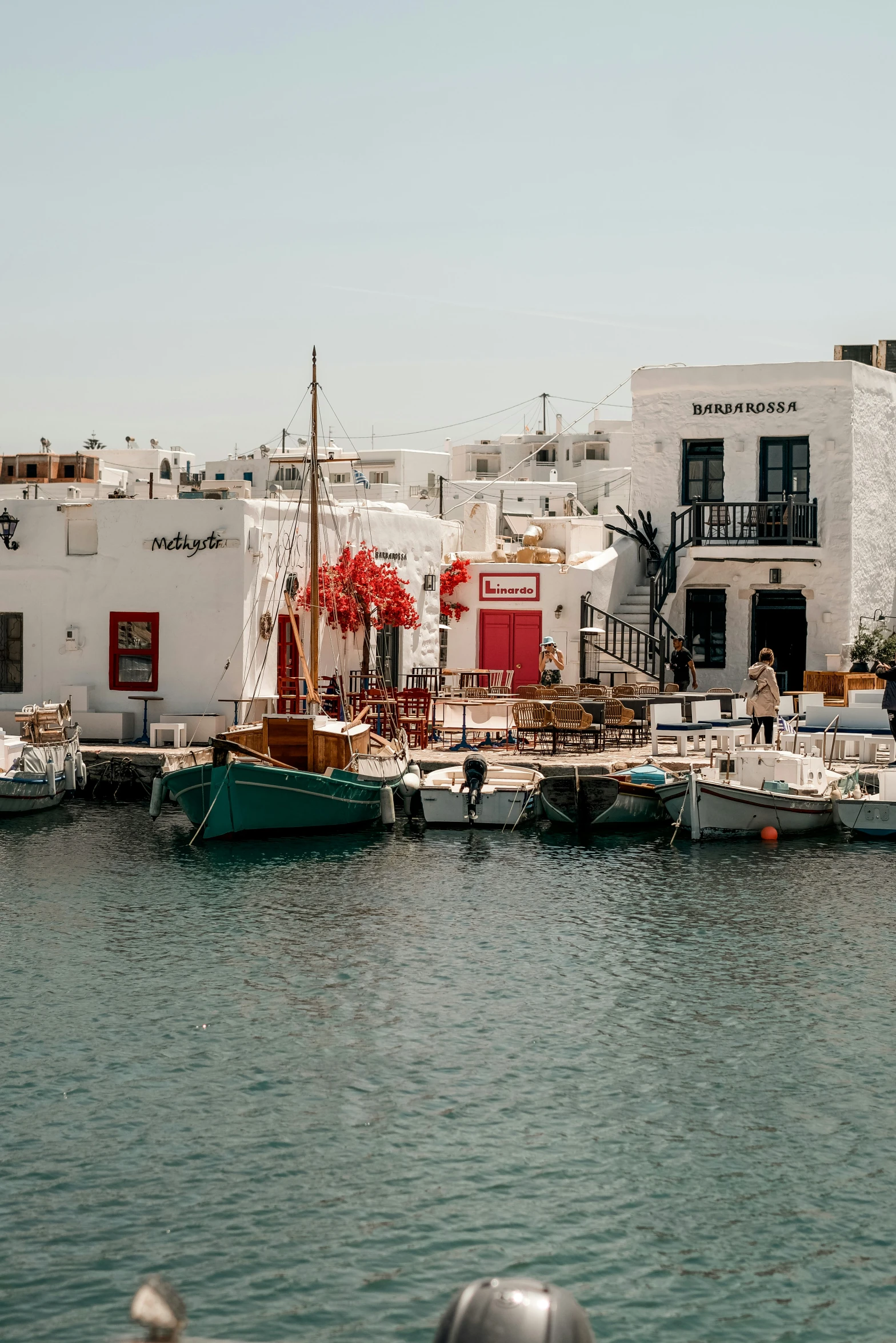 several boats sit in the water with buildings behind them