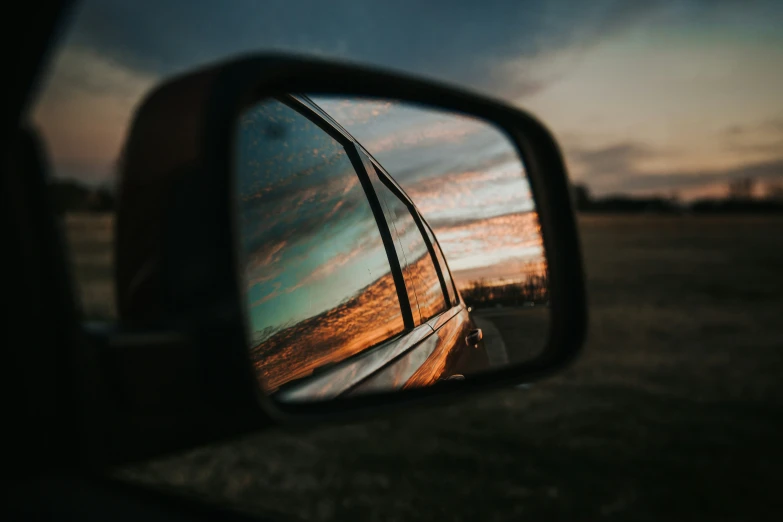 a rear view mirror showing an orange sunset in the background