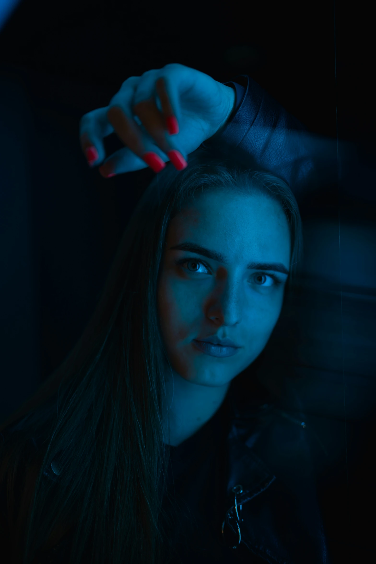 a woman in a leather jacket holds her hair and stares at the camera