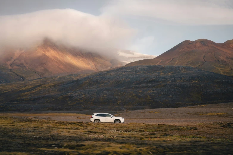 white car parked on desert terrain with mountains in background