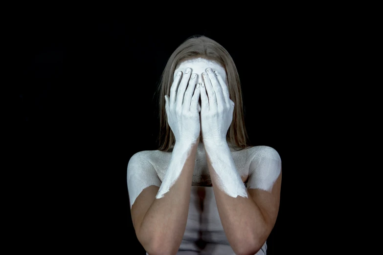 woman wearing white makeup and her hands covering her face