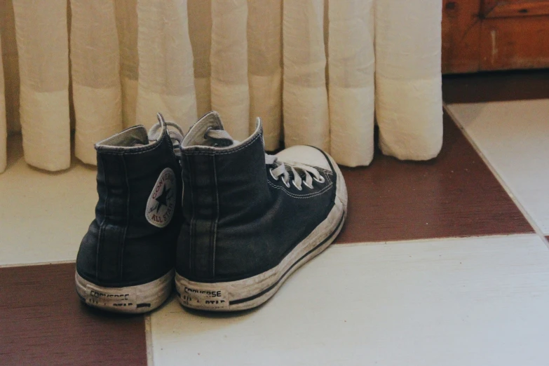 a pair of black converse style sneakers sitting on a tile floor