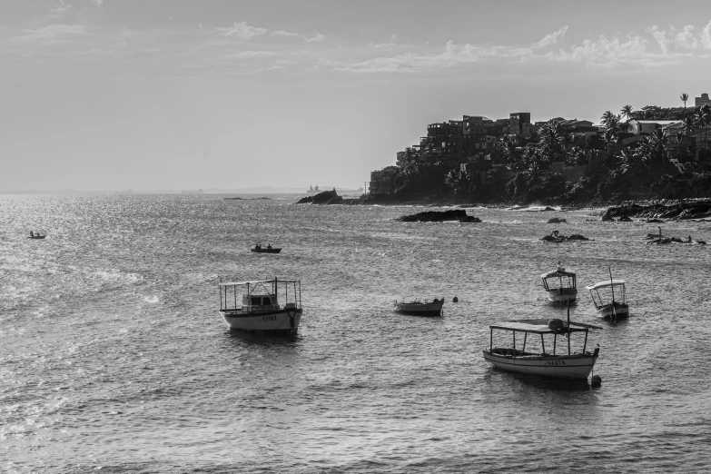 a bunch of boats floating in the ocean near a hill