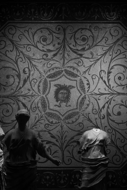 two statues are looking down on a wall with intricately designed designs