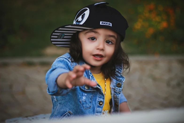 little girl wearing a black hat and blue denim jacket pointing
