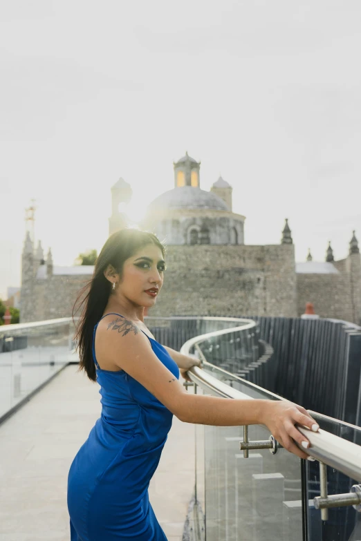 a young woman in blue dress leaning on a railing