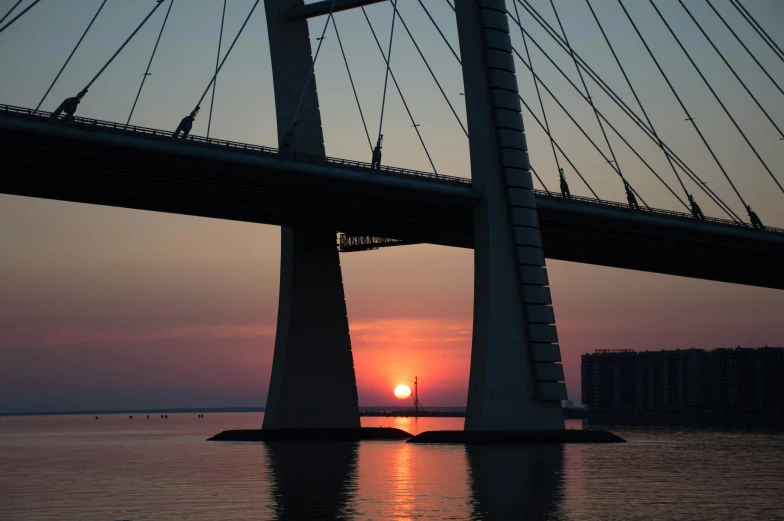 the sun is setting behind an impressive bridge