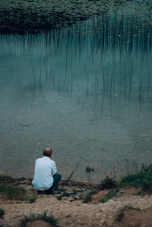 a man sitting by the water with a fishing pole