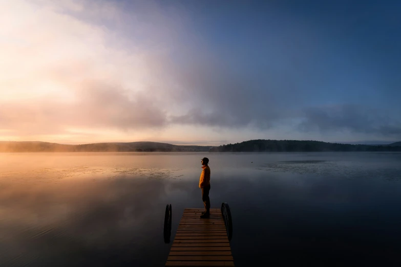 man standing on a dock in the morning looking out over a lake