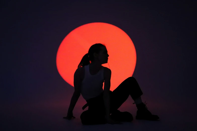 girl with backpack sitting in front of orange and black sun