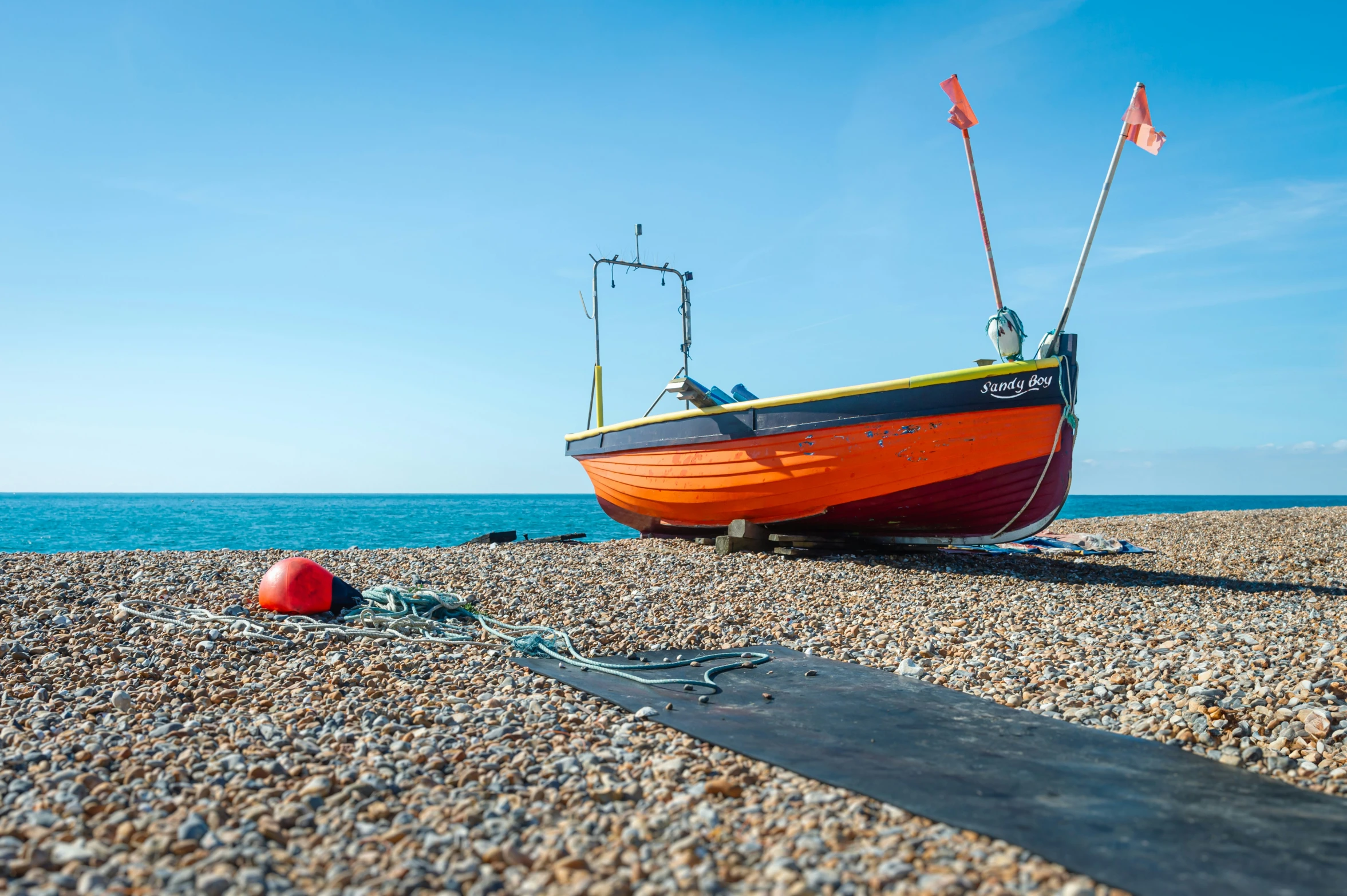 a orange boat sitting on a rocky beach near the water