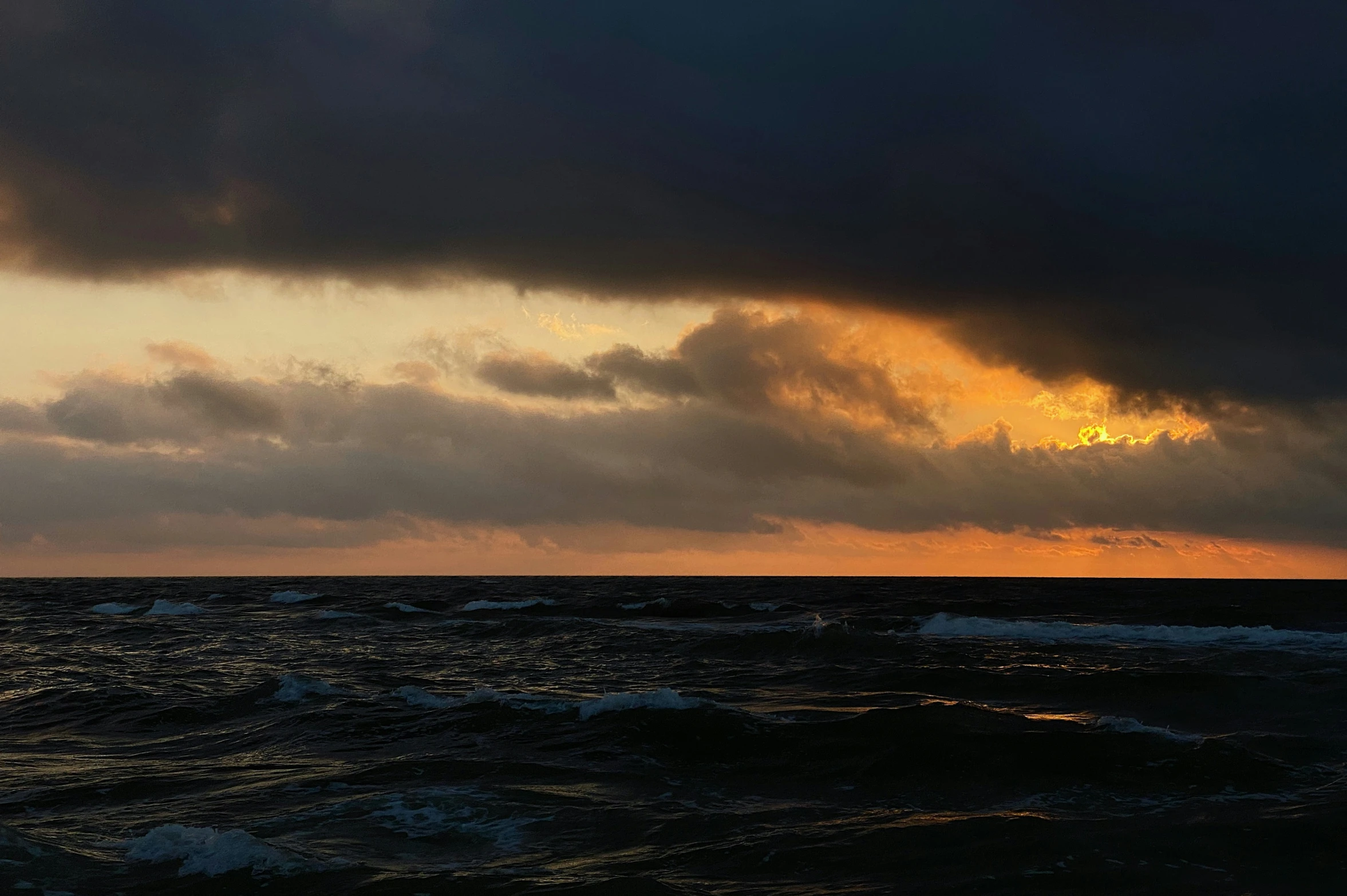 dark clouds are rising over the ocean near a body of water