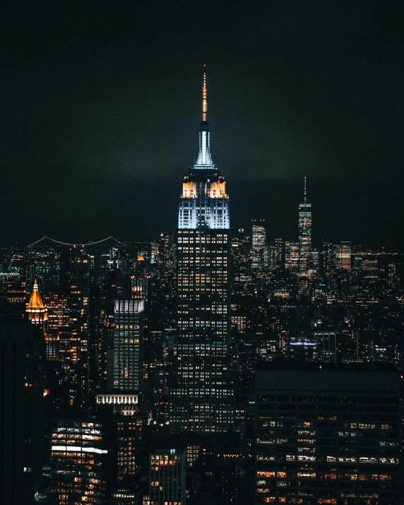 the empire building rises above new york city's downtown skyline at night