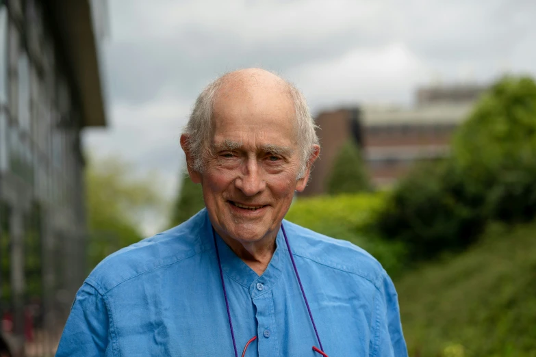 a man with grey hair wearing a blue shirt and string necklaces