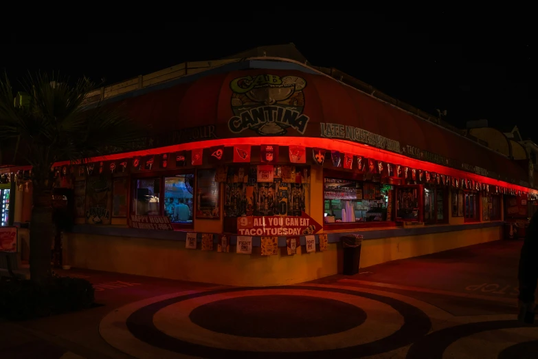 a street side view of a large restaurant with some advertits on the building and lights up at night
