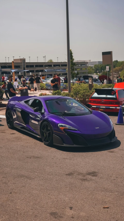 a supercar sits in a parking lot as spectators walk in front