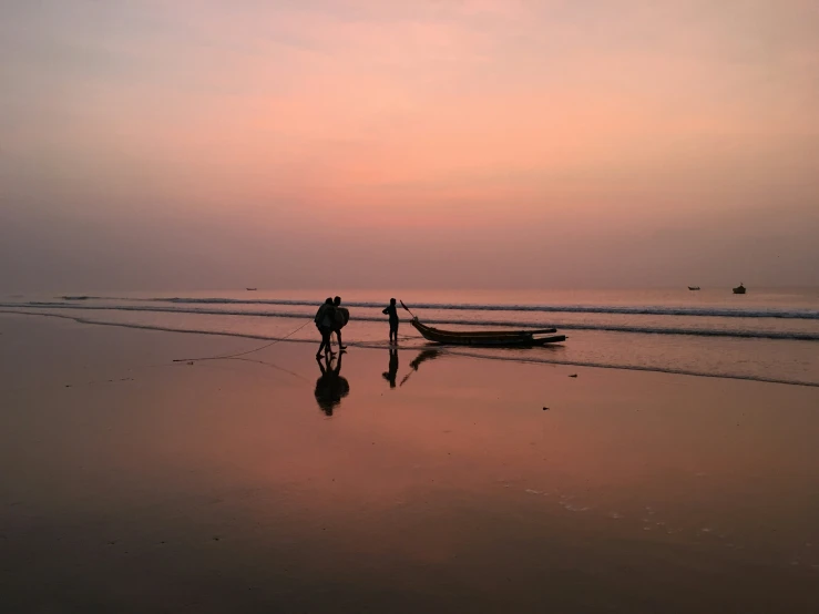 two people are standing on the beach with their boats