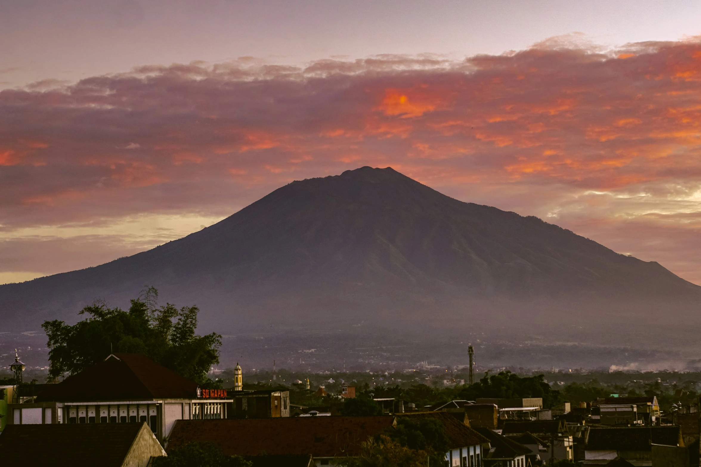 pink and orange clouds above some houses and a hill