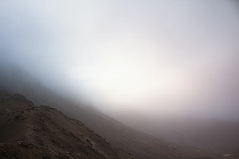 a mountain side is obscured by fog and a person skiing on the slopes