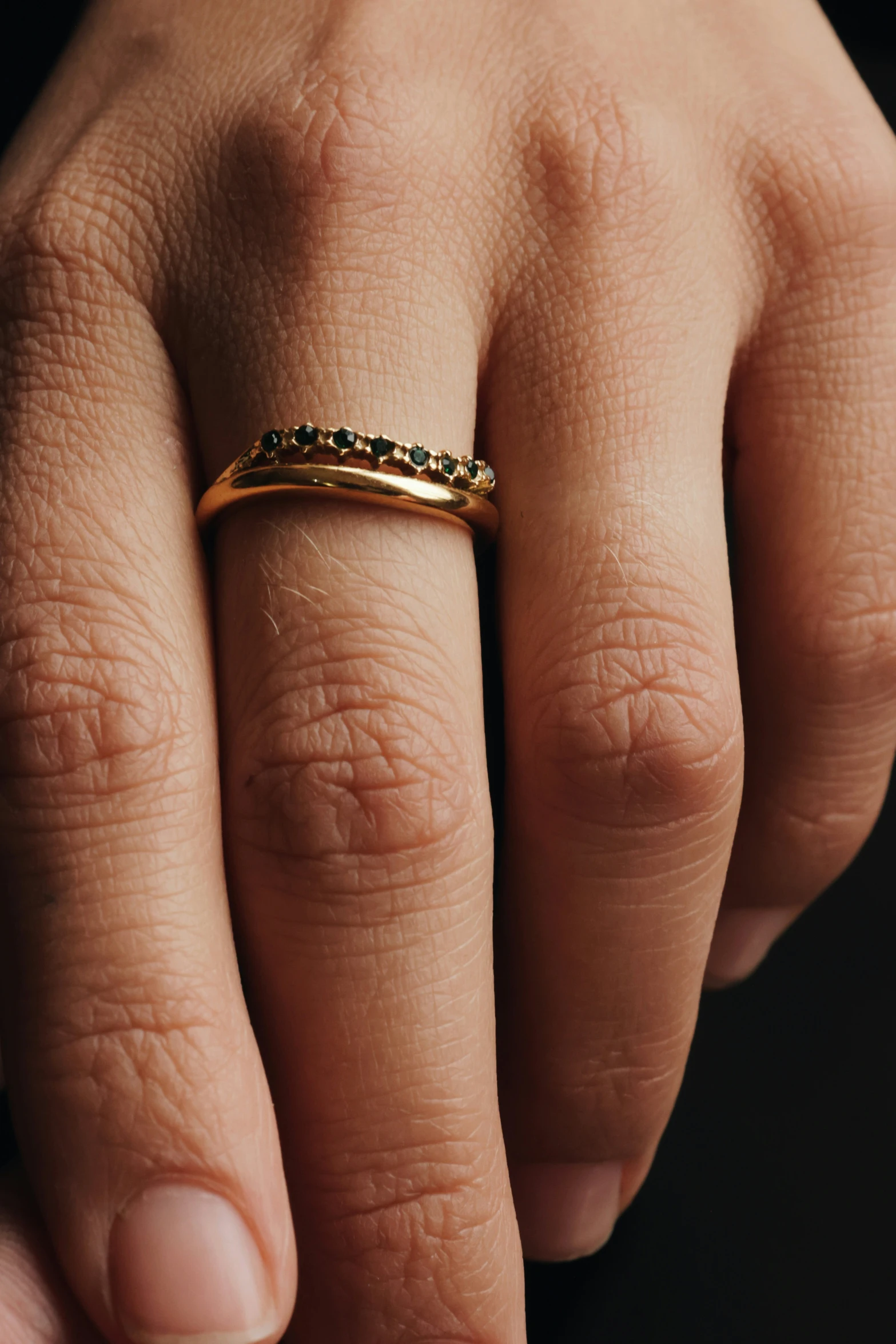 the gold ring features tiny black stones and stands on a persons hand