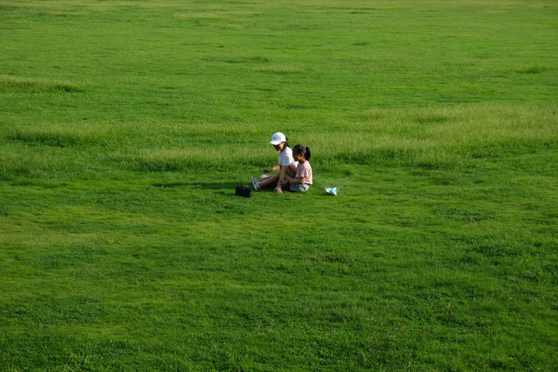 two women sit together on a large grass field