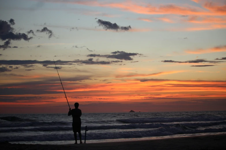 a person fishing from a beach as the sun goes down