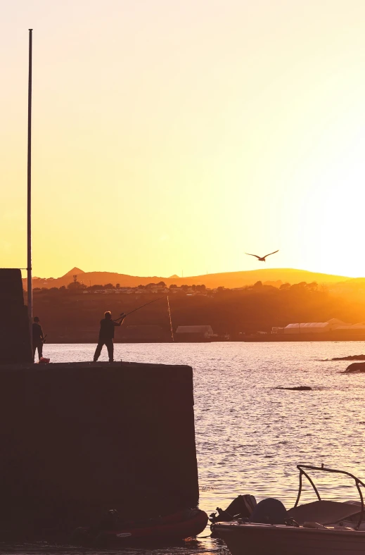 two people are fishing at a harbor at sunset