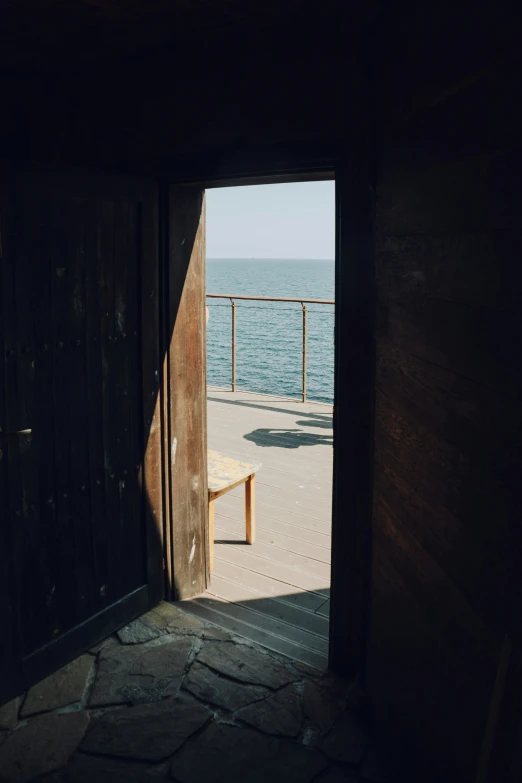 a lone bench sitting on the edge of an open doorway by the ocean